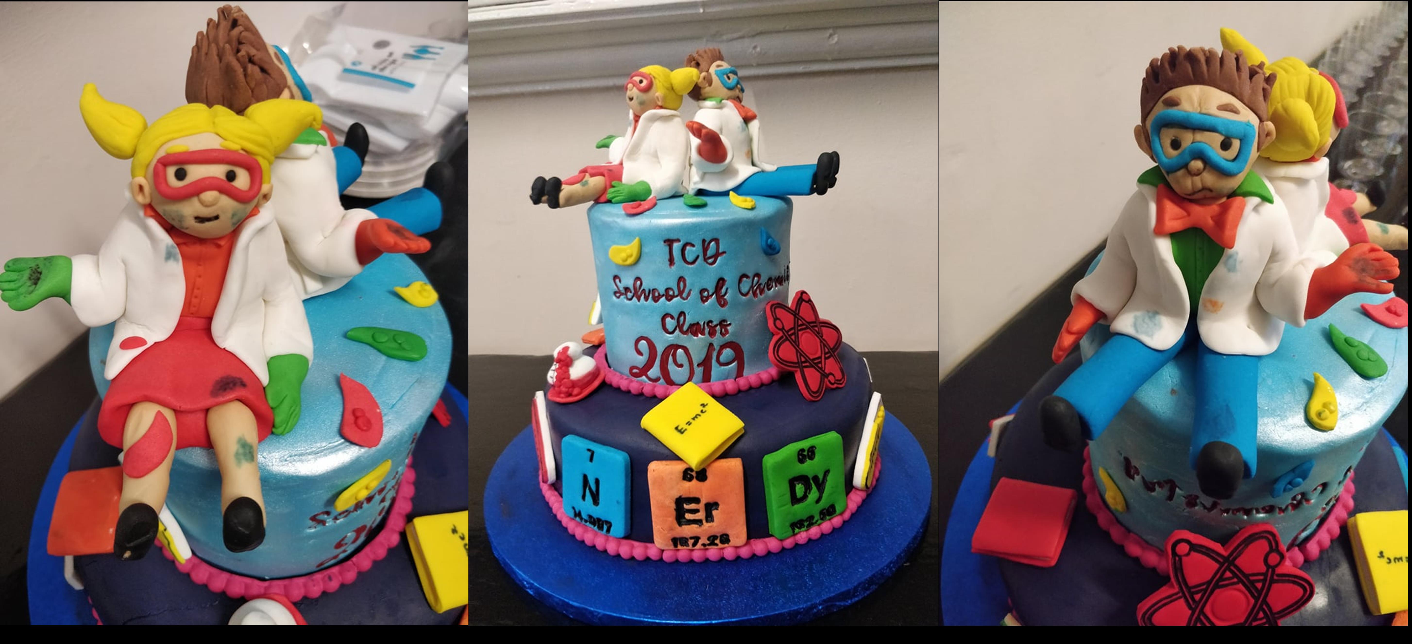 A cake Decorated with Science symbols and books and topped with Two scientists made from sugarpaste